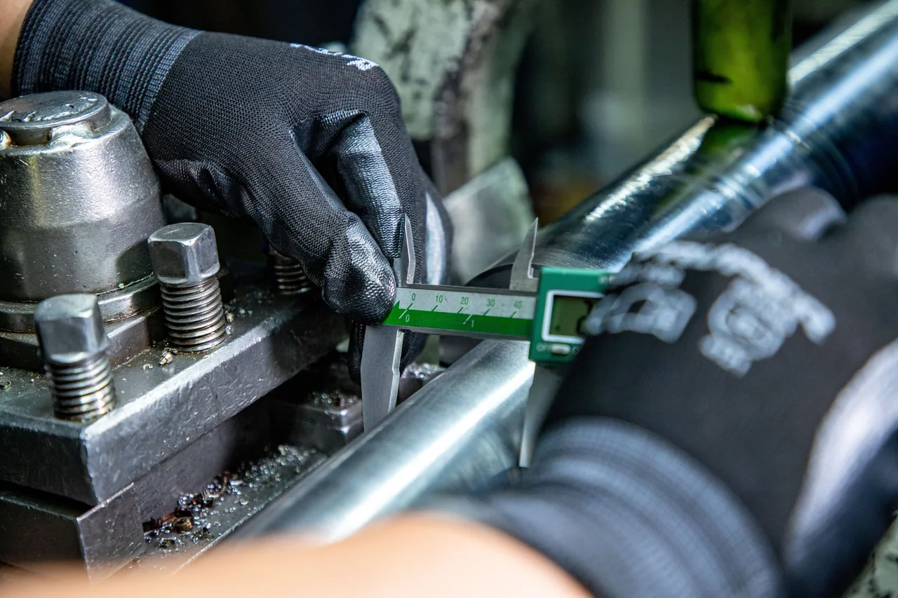 Technician measuring a machined metal component with a digital caliper